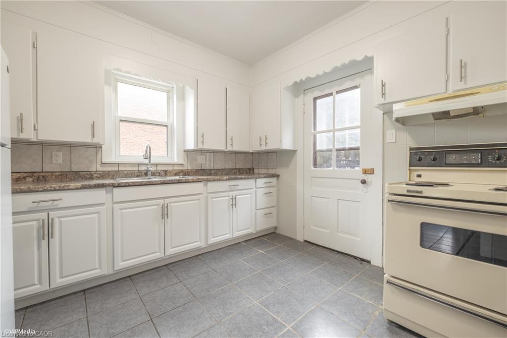 White cabinetry, tile backsplash, laminate countertops, stainless steel sink, and tile flooring