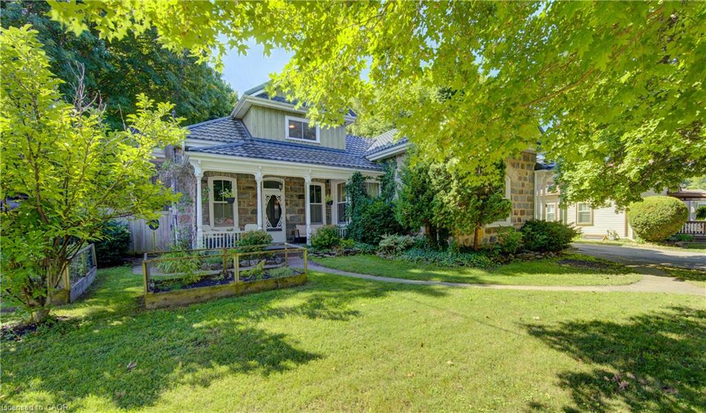 Stone exterior with a covered porch, gabled dormer, dark-toned roof, and a front yard with mature landscaping