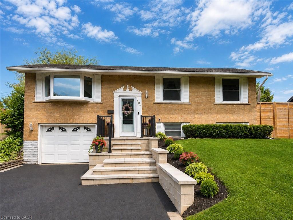 Brick facade residence featuring an attached garage, bay window, landscaped front yard with block retaining walls, and a paved driveway