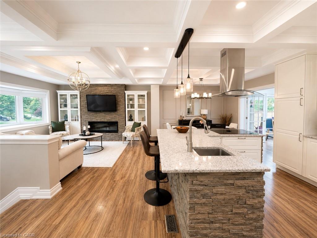 Open-concept living space featuring wood-finish flooring, a stacked stone kitchen island with a double basin sink, and a coffered ceiling