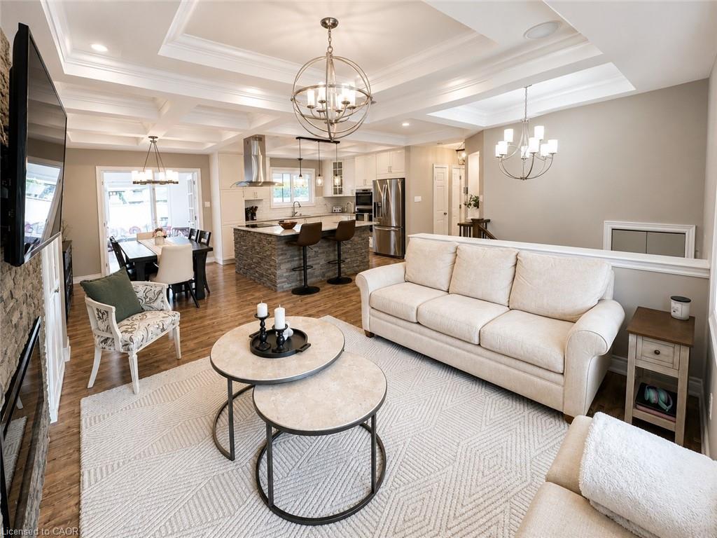 Open-concept living space featuring coffered ceilings, wood-finish flooring, and a stacked stone fireplace surround
