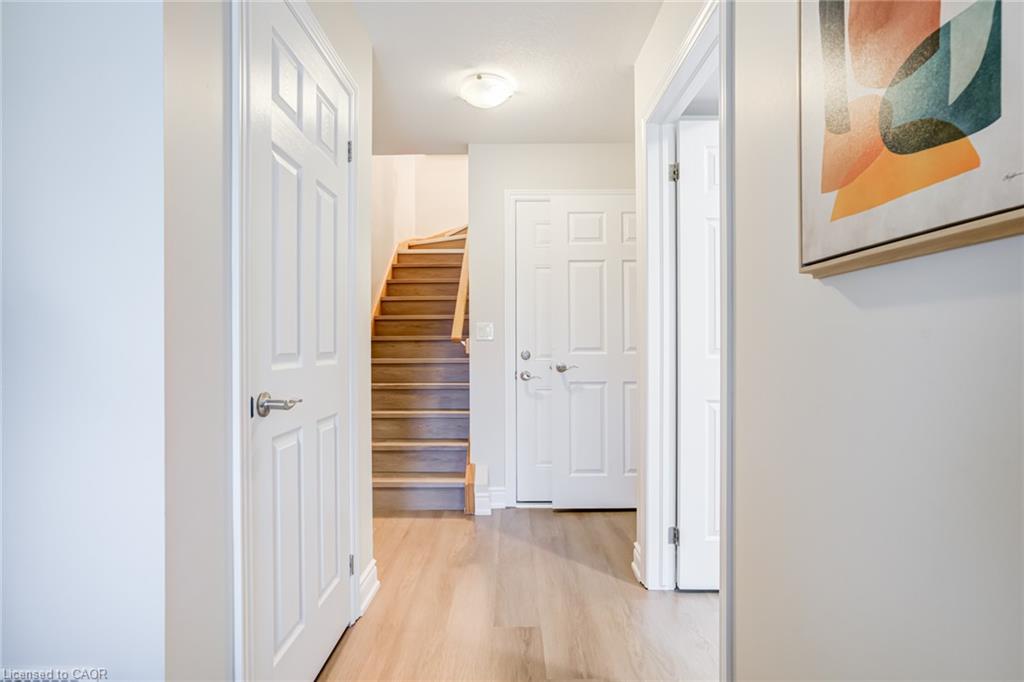 Hallway featuring wood-finish flooring, white panel doors, and a wood staircase with a matching handrail