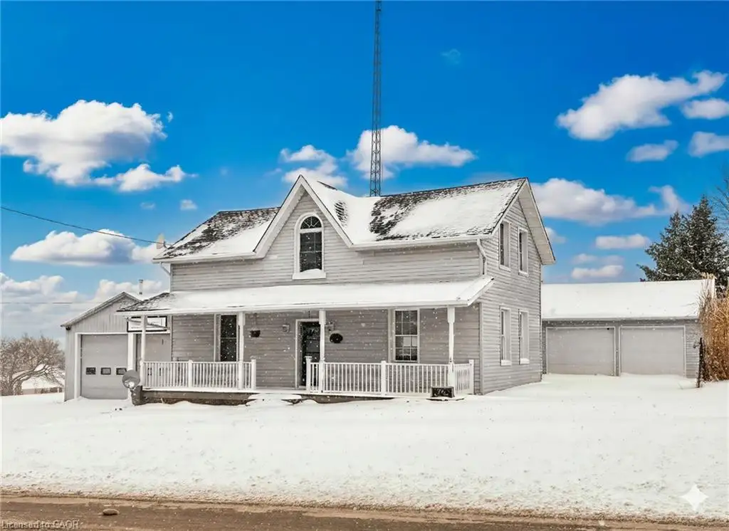 Traditional two-story home featuring a covered front porch with white railing, a dormer window, an attached single-car garage, and a detached two-car garage