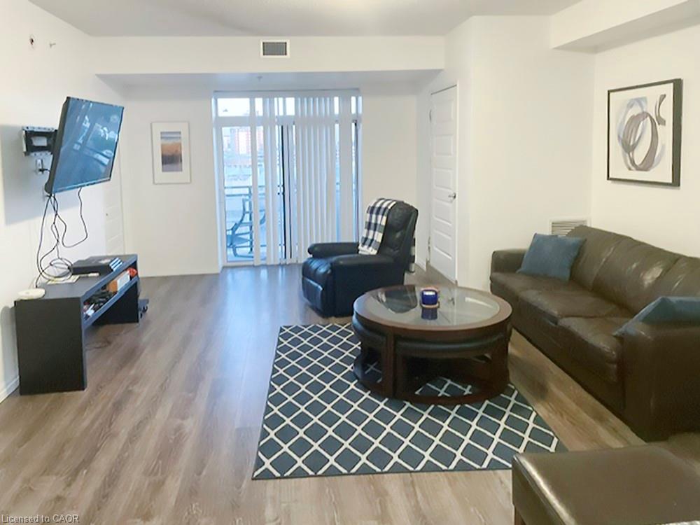 Open-concept living area featuring wood-finish flooring, white walls, and a glass-paneled sliding door opening to a private balcony