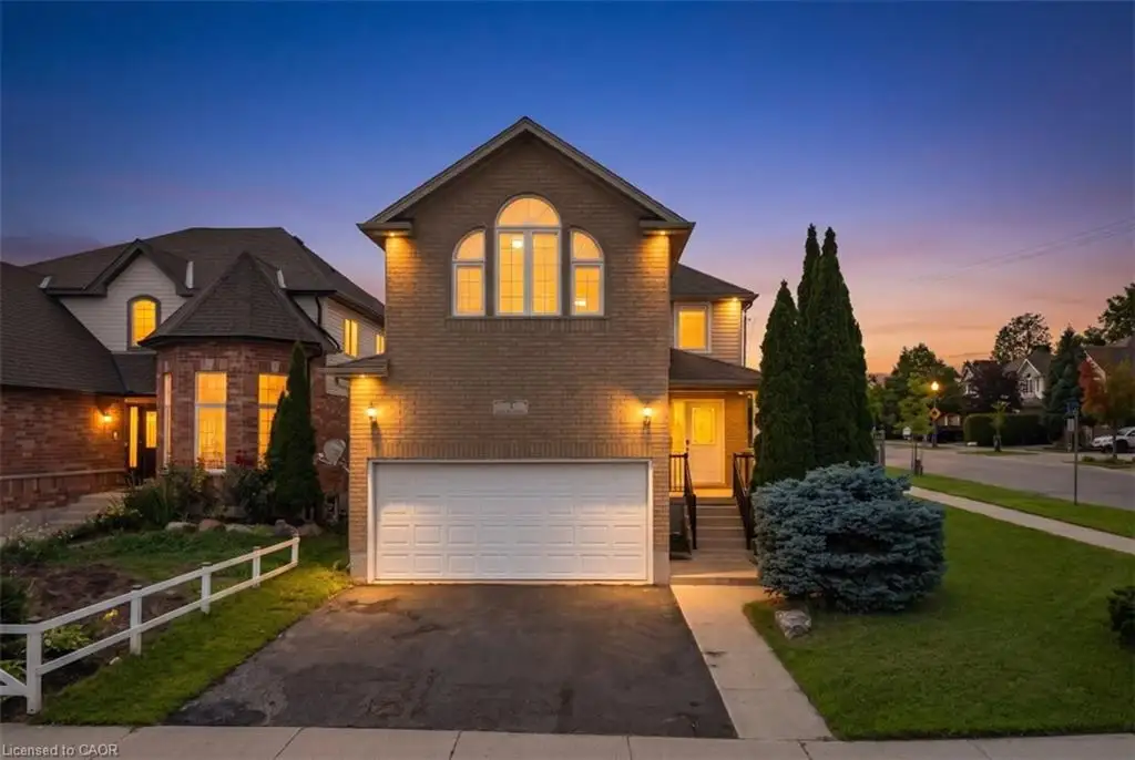 Brick exterior with arched windows, attached garage, paved driveway, and manicured landscaping