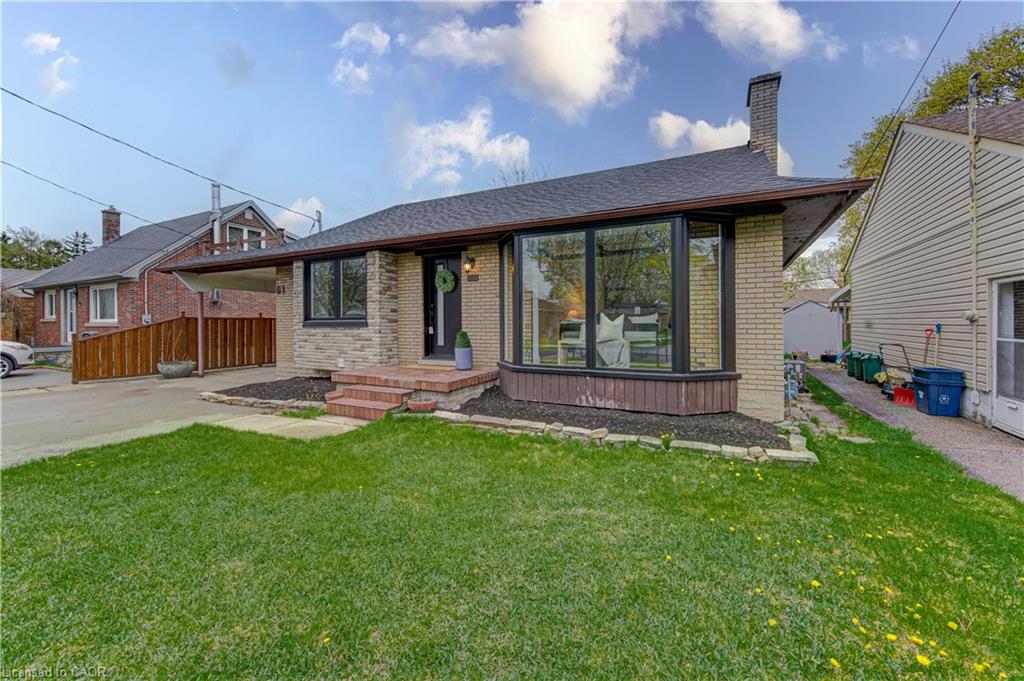 Bungalow residence featuring a stone and brick facade, a prominent bay window, a covered carport, and a dark shingle roof