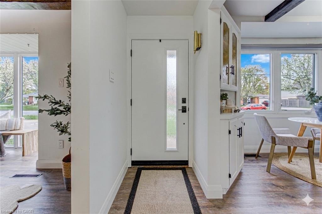 Entryway featuring a white door with frosted glass insert, wood-finish flooring, and a built-in white cabinet with glass-front upper doors and matte black hardware