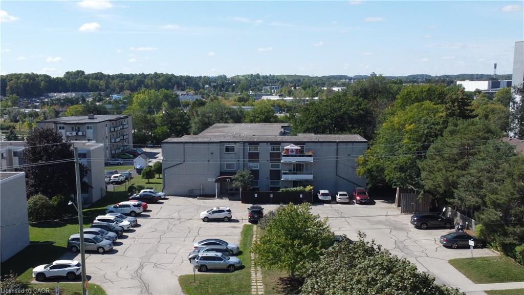 Multi-story residential building with exterior balconies, on-site surface parking, and surrounding mature trees