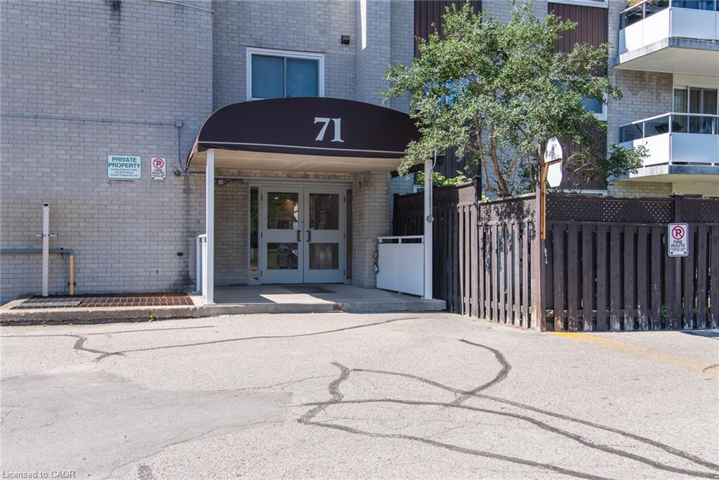 Building entrance featuring a brown awning, double glass doors, light brick exterior, and a wooden privacy fence
