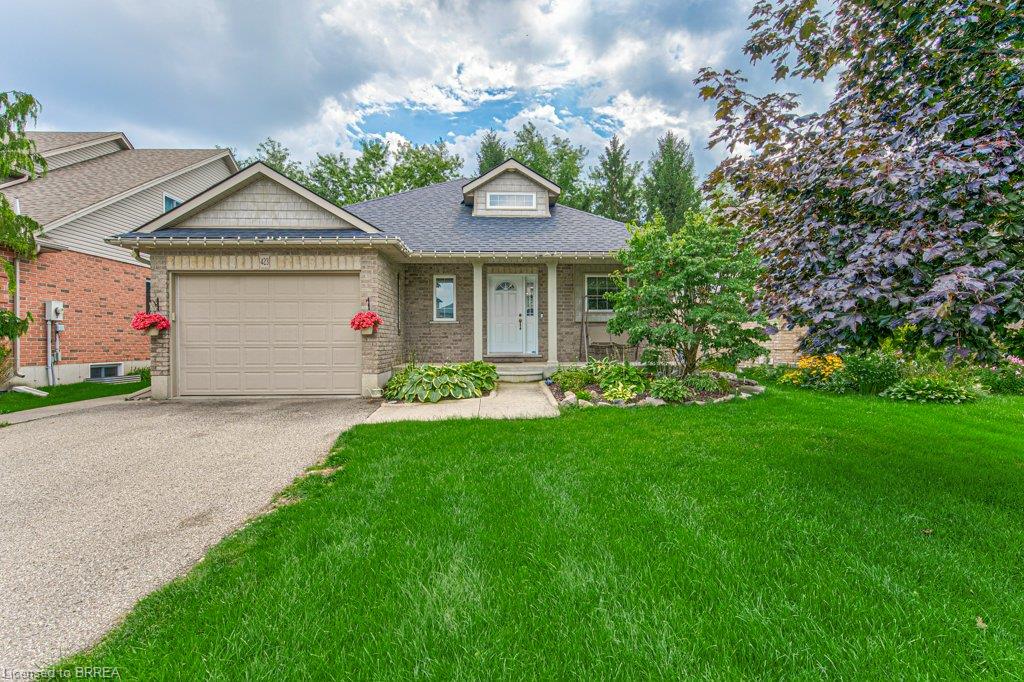 Brick exterior with decorative dormer, attached garage, and mature landscaping
