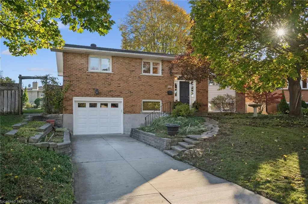 Brick exterior featuring an attached single-car garage, concrete driveway, stone-retaining wall landscaping, and mature trees
