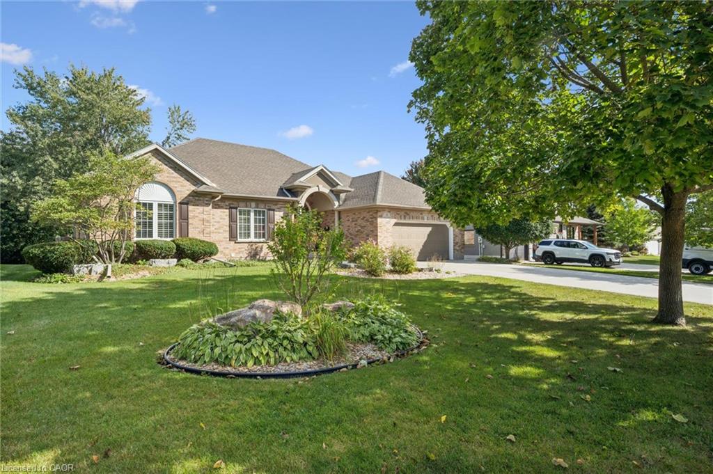 Brick exterior, arched window, brown shutters, attached garage, well-maintained lawn, and mature trees