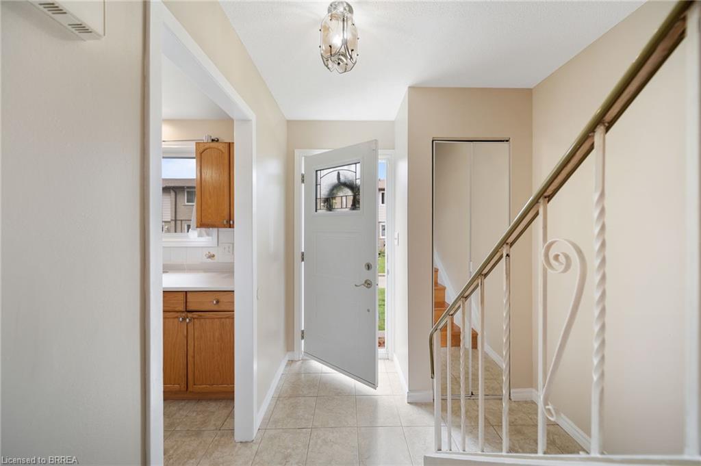 Tiled entryway flooring with a decorative overhead light fixture, leading to a staircase with a metal handrail and balusters, and a kitchen featuring wood cabinetry and light-toned countertops