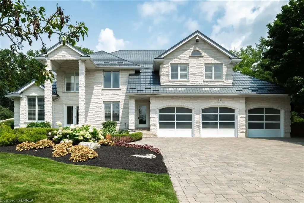Stone veneer exterior featuring a three-car garage with arched glass panel doors, a metal tile roof, and a paver driveway