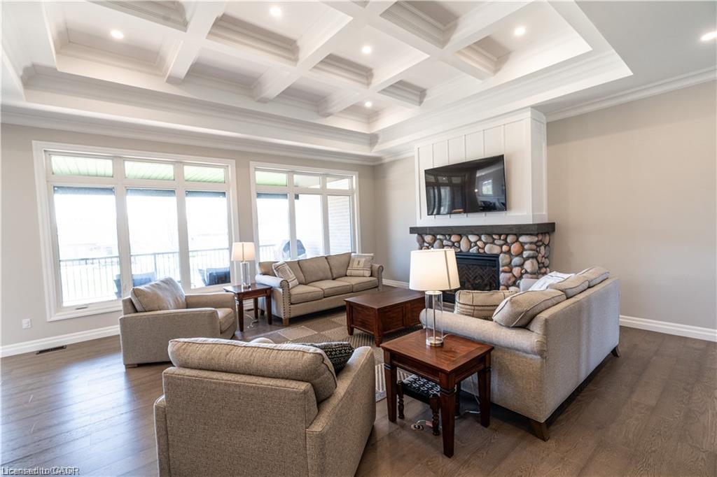 Spacious living area featuring a coffered ceiling with recessed lighting, a stone-surround fireplace with a dark mantel, and wood-finish flooring