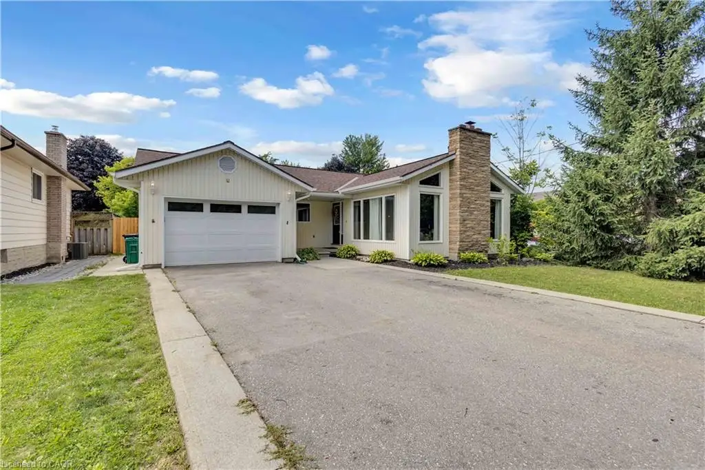 Attached two-car garage, stone-clad chimney, large picture windows, and mature trees framing the property