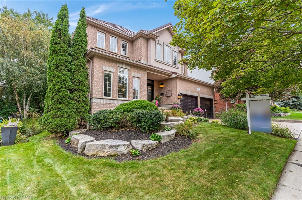 Brick and stucco exterior, arched two-car garage doors, terraced landscaping with rock accents, mature trees, and an established front lawn