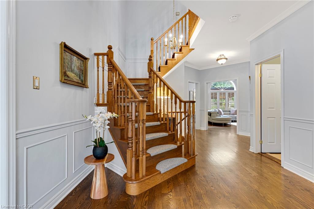 Grand wooden staircase with carpeted treads, wood-finish flooring, wainscoting details, and a decorative ceiling light fixture