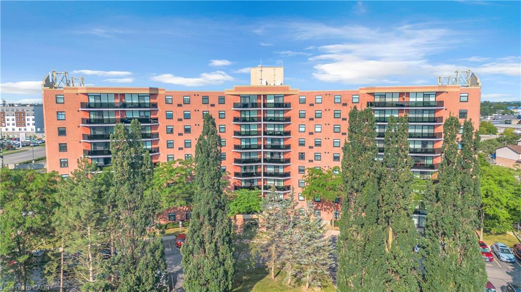 Brick facade, multiple stories, numerous balconies with dark railings, many windows, surrounding mature trees
