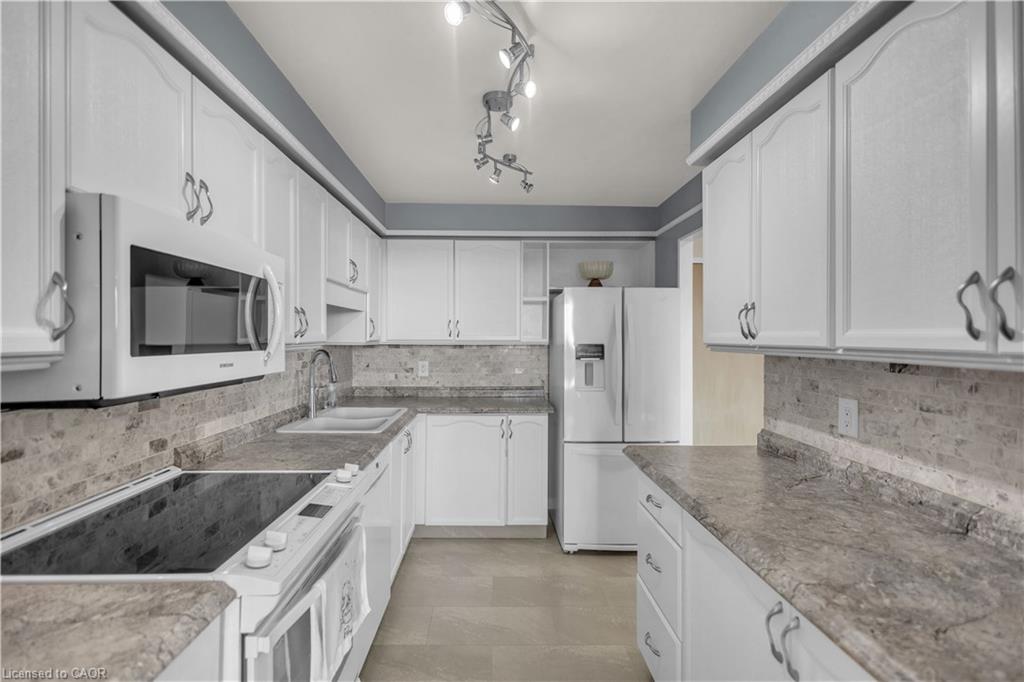 White cabinetry with decorative hardware, stone-look countertops, tiled backsplash, built-in microwave, and track lighting