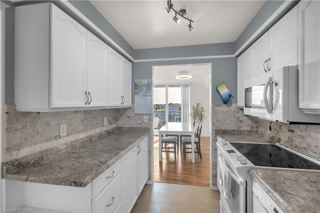 White cabinetry with silver hardware, stone-finish countertops, stone tile backsplash, and stainless steel microwave