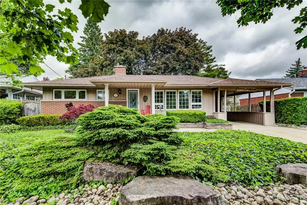 Ranch-style exterior with brick detailing, covered carport, front porch entry, white-framed windows, and a landscaped front yard with mature plantings