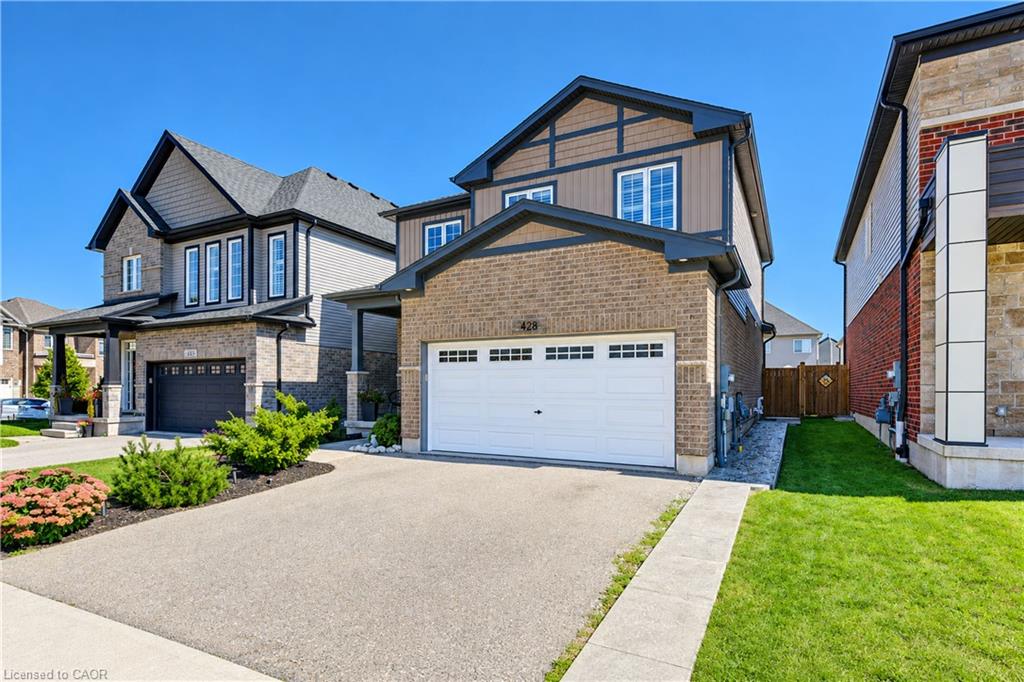 Brick and siding facade with dark trim accents, attached garage with white door, concrete driveway, and well-maintained front landscaping