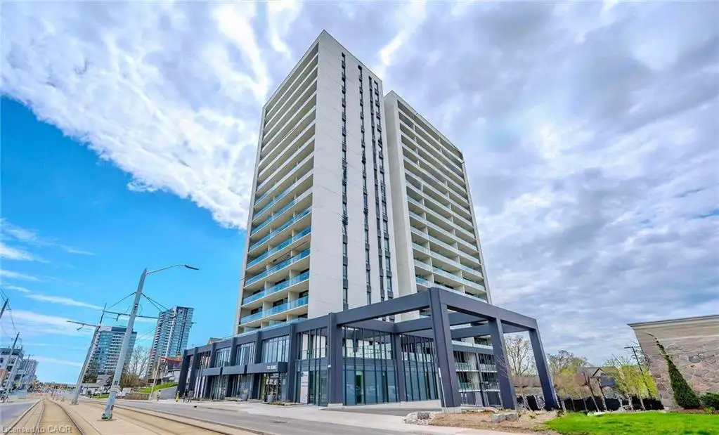 High-rise residential building featuring a concrete exterior, glass-paneled balconies, floor-to-ceiling windows on the ground level, and a prominent dark-toned steel structural frame at the entrance