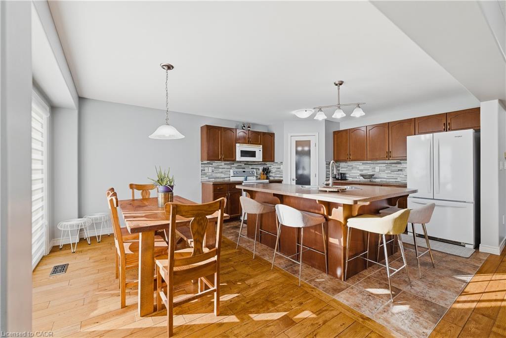 Kitchen with light countertops, brown cabinetry, white appliances, hanging light fixtures, and light wood-type flooring