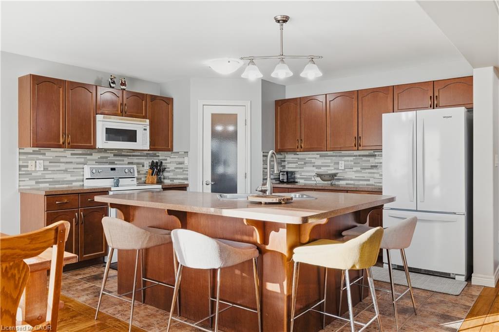 Kitchen with pendant lighting, white appliances, brown cabinetry, light countertops, and a center island with sink