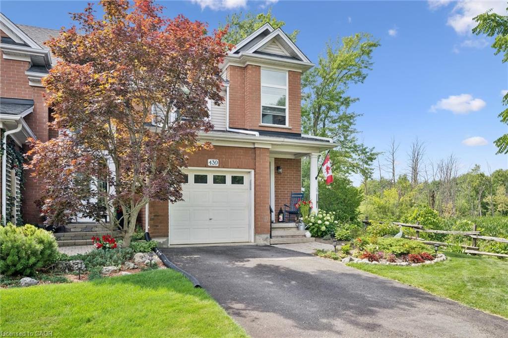 Brick exterior with a covered front porch, white garage door, paved driveway, and mature landscaping