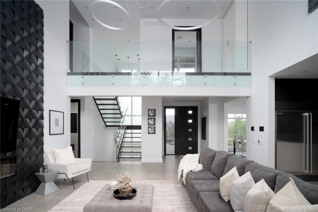 Two-story living area featuring a prominent textured accent wall, concrete-finish flooring, glass panel railing, open-tread staircase with metal railing, and a large stainless steel refrigerator