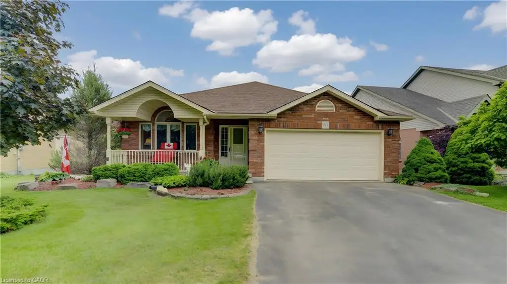 Brick facade residential property featuring a covered front porch with white railings, an attached two-car garage with a light-colored door, a paved driveway, and a front lawn with established landscaping