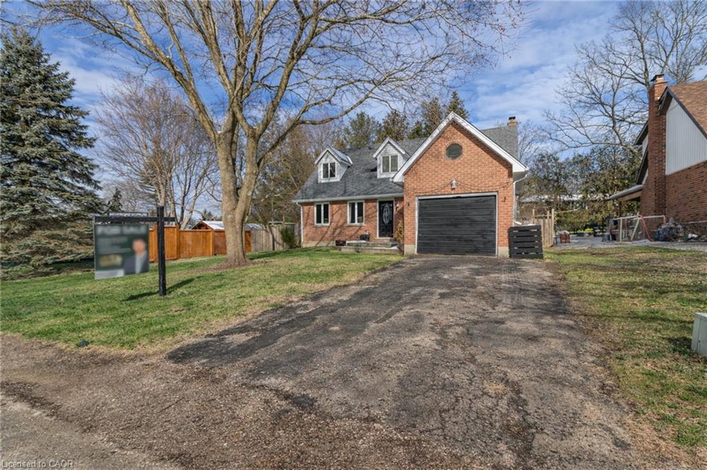 View of front of house featuring brick siding, driveway, a chimney, and a garage