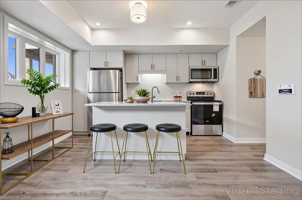 Stainless steel appliances, recessed lighting, wood-finish flooring, white cabinetry, and a kitchen island with seating
