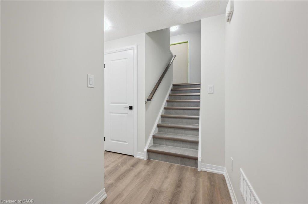 Wood-finish flooring, staircase with tile treads, white interior doors, and contemporary wall-mounted lighting