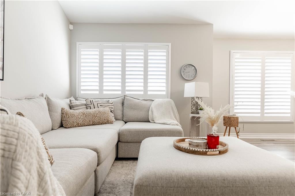 Recessed lighting, large windows with white louvered shutters, and light wood-finish flooring