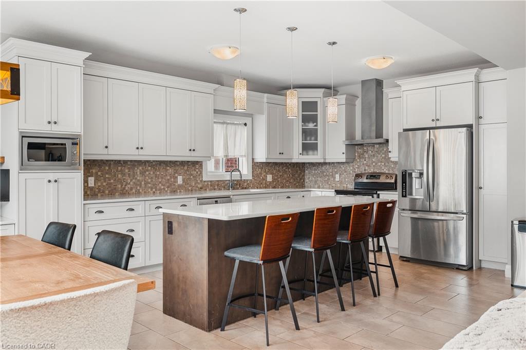 Kitchen with appliances with stainless steel finishes, a kitchen bar, a kitchen island, wall chimney range hood, and backsplash