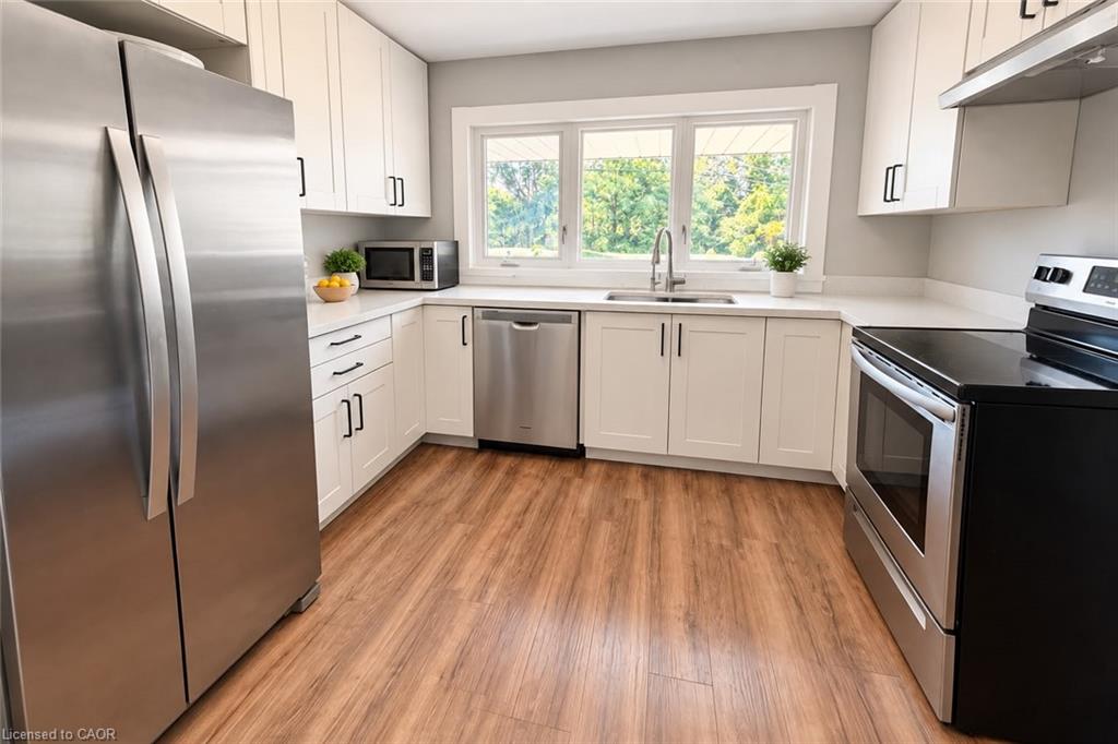 Kitchen featuring wood-finish flooring, white cabinetry with black hardware, stainless steel appliances, and a solid surface countertop