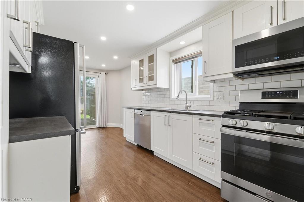 Kitchen featuring wood-finish flooring, white cabinetry, dark countertops, a white subway tile backsplash, and stainless steel appliances