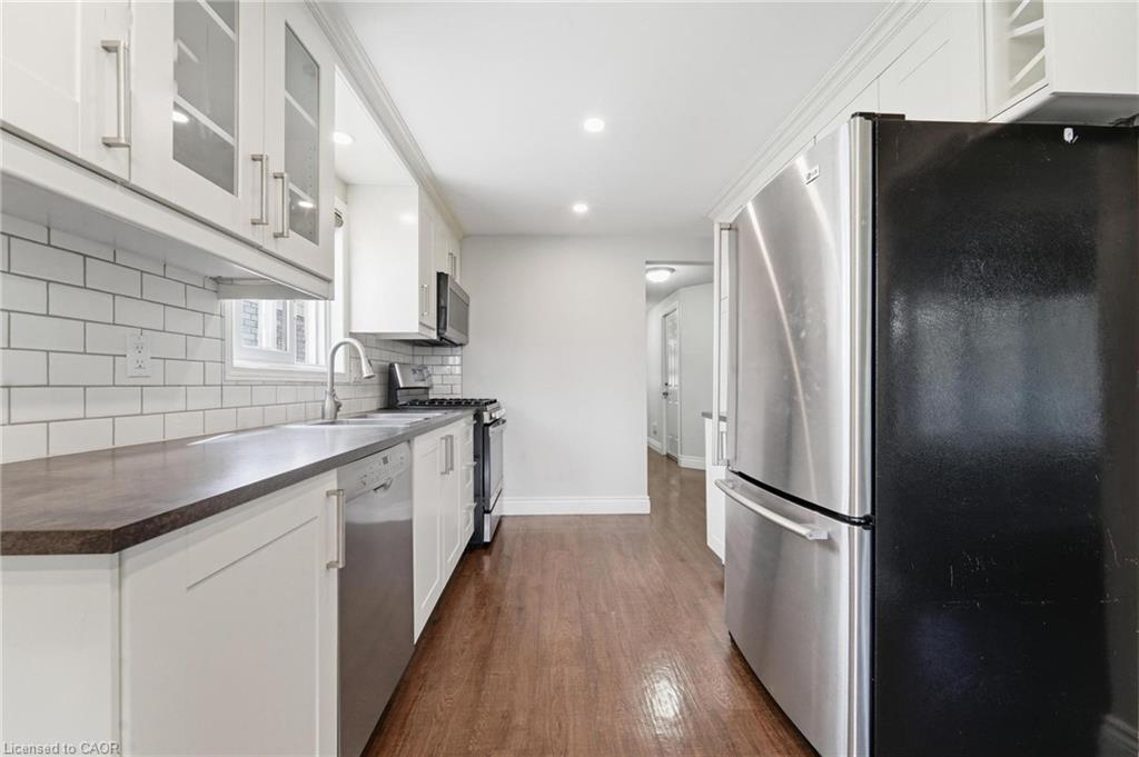 White cabinetry with glass-front uppers, stainless steel appliances, dark countertops, white subway tile backsplash, and wood-finish flooring
