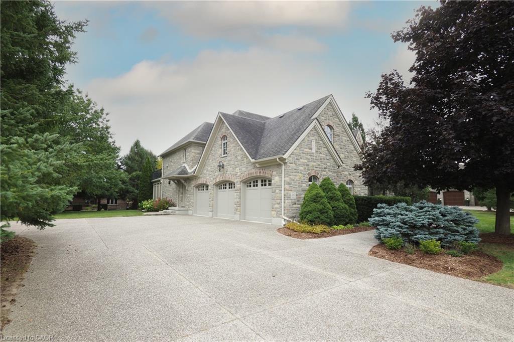 Stone veneer exterior, multi-gabled roofline, triple garage with individual doors, exposed aggregate driveway, and established landscaping