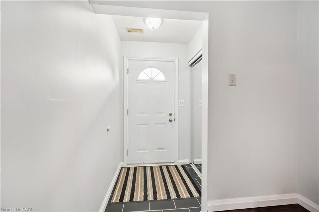 White paneled entry door with an arched transom window, recessed ceiling light, and dark tile flooring