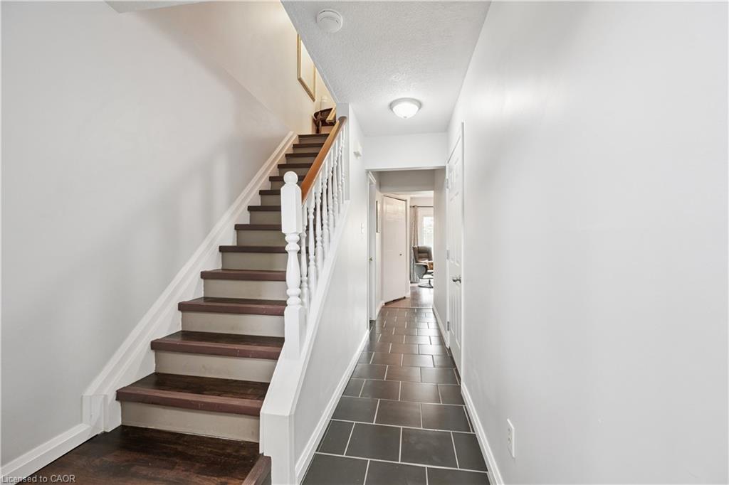 Hardwood stair treads with white risers and balusters, dark tile flooring in hallway, and flush-mount ceiling lighting