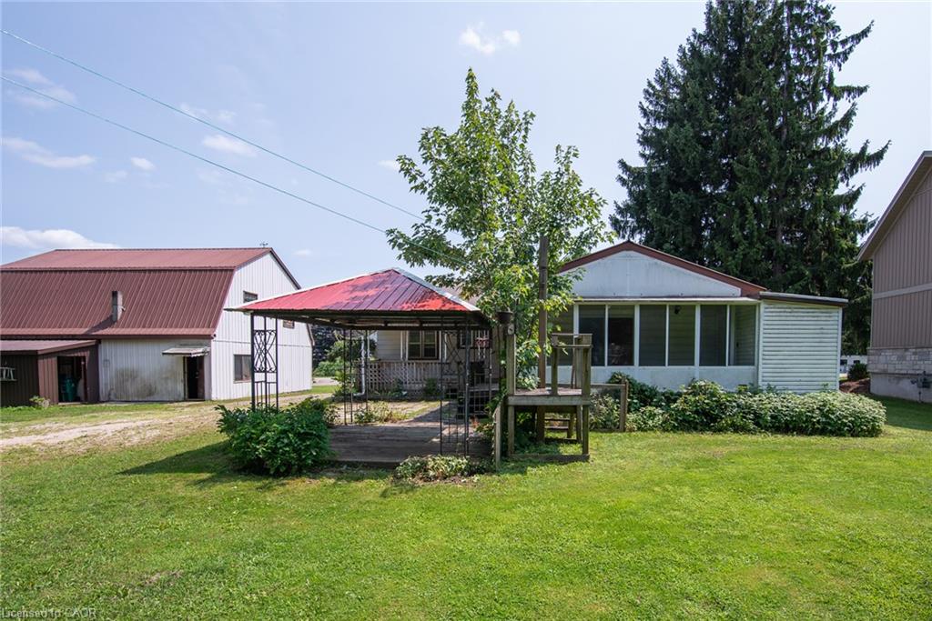 Spacious grounds featuring mature landscaping with evergreen and deciduous trees, manicured lawn, and multiple outbuildings including a metal-roof structure and detached residences with siding exteriors