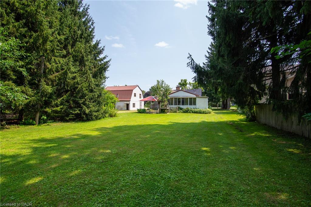 Expansive green lawn with mature evergreen trees and a white structure featuring a screened porch
