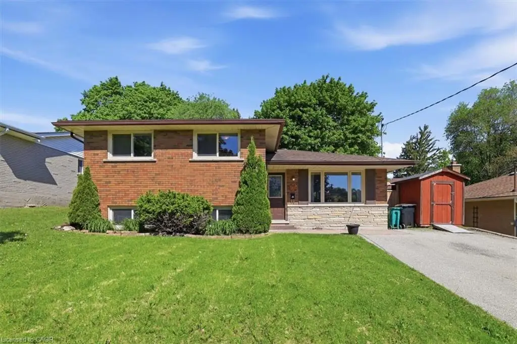 Brick exterior with stone accents, mature landscaping, paved driveway, and detached storage shed