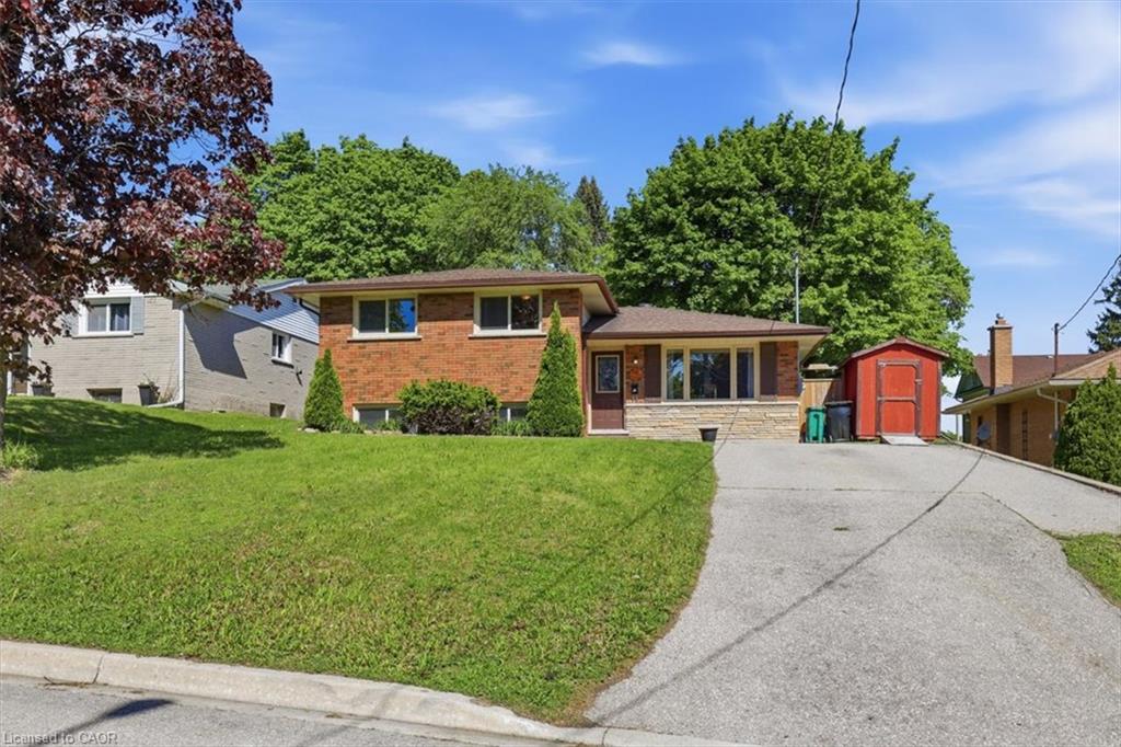 Brick exterior with stone accents, a sloped driveway, and a red storage shed