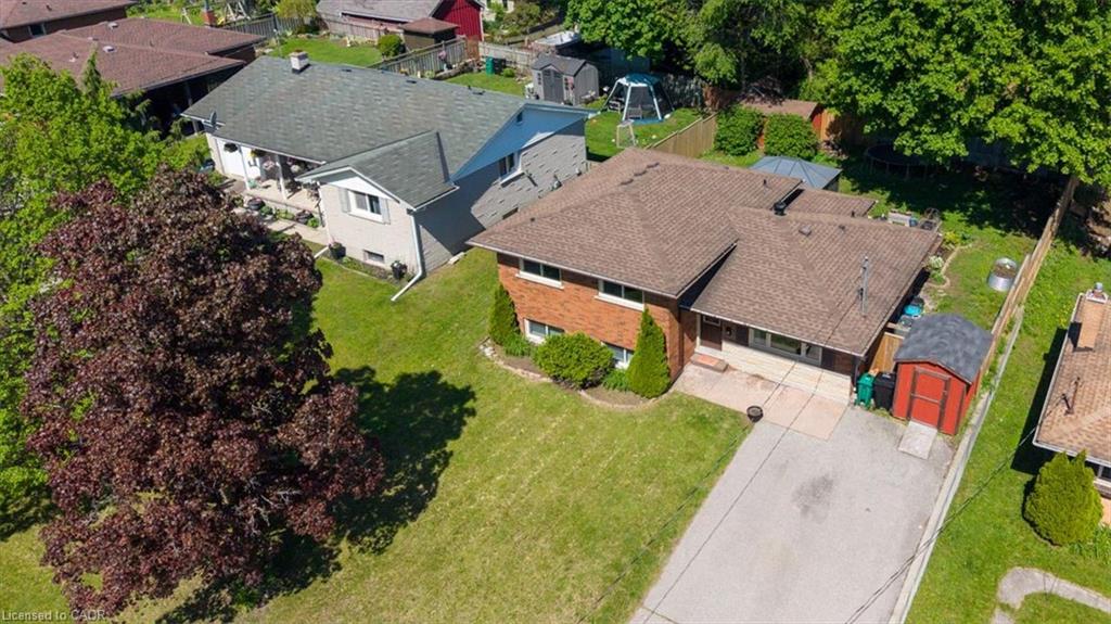 Brick exterior residence with a brown shingle roof, paved driveway, and a detached storage shed