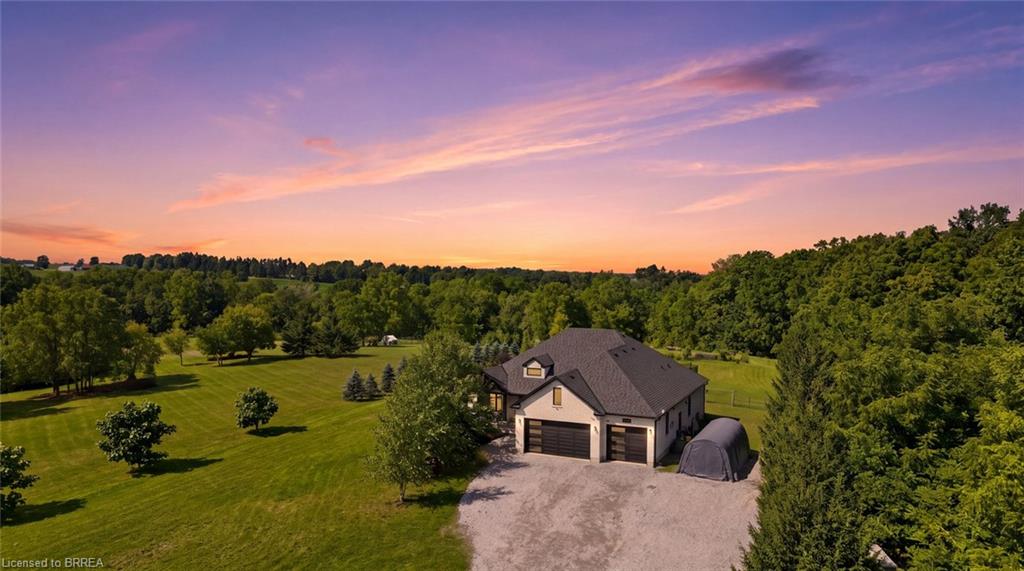 Expansive property featuring a gravel driveway, attached two-car garage, and a lush, tree-lined landscape